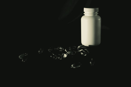 Omega-3 fish oil capsules spilled from bottle, copy space. Omega3 gel capsules on black background....