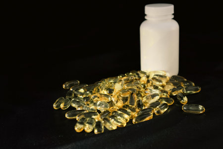 Omega-3 fish oil capsules spilled from bottle, copy space. Omega3 gel capsules on black background....