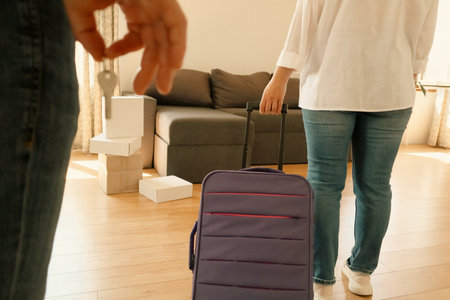 Close-up of a man holding house keys and a woman pulling a suitcase inside a new apartment. Concept of moving in, new home, renting, real estate, relocation, or starting a new life together.の写真素材