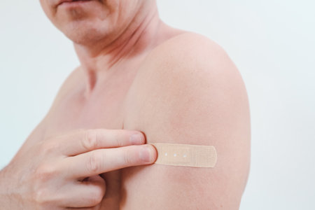A man's upper arm with a small adhesive bandage applied after receiving a vaccine or injection....