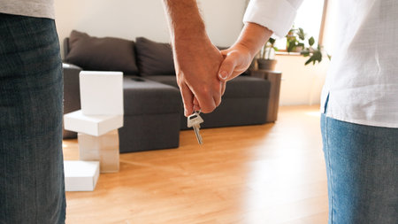 Close-up of a couple holding hands with house keys in a bright living room. Symbol of new home...