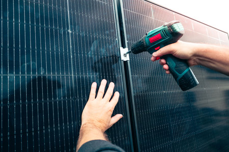 Close-up shot of a technician's hands using a battery-powered drill to attach a mounting bracket to a black solar panel. Focus on installation and assembly process of renewable energy systems.の写真素材