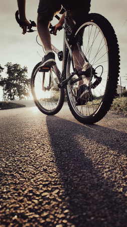 Low-angle view of a cyclist riding along a country road at sunset. Concept of freedom, adventure, healthy lifestyle, outdoor sports, and evening cycling.の写真素材