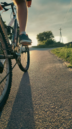 Low-angle close-up of a cyclist pedaling along a rural road at sunset. Symbol of freedom, adventure, fitness, healthy lifestyle, and outdoor activity.の写真素材