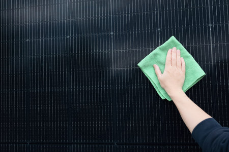 Close-up of a person's hand using a green microfiber cloth to clean the surface of a black solar panel. Essential maintenance and care for effective renewable energy generation and sustainability.の写真素材