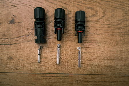 Overhead view of several disassembled MC4 connectors, showing the black plastic bodies and the metal pin and socket contacts required for connecting solar panel wiring, placed on a light wooden backgrounds and metal contacts on a wooden surface.の写真素材
