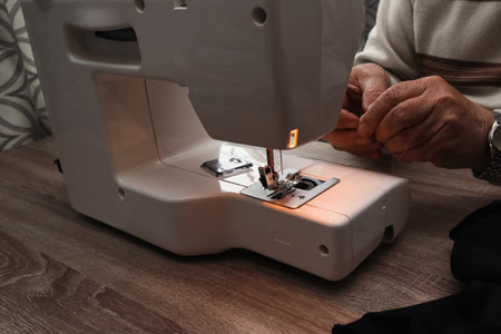 A close-up of an elderly person's hands carefully threading a needle on an electric sewing machine....