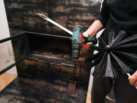 A man in front of a wood-burning fireplace holding a soot cleaning kit and a drill. Home...