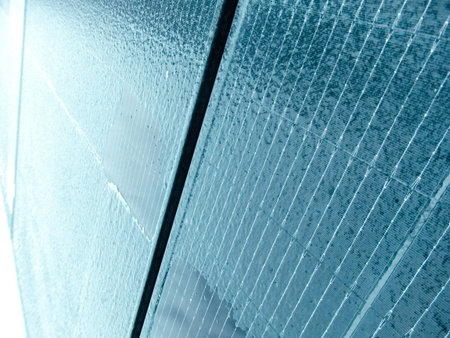 A close-up, angled view of a blue photovoltaic panel covered in frost and melting ice. Highlights...