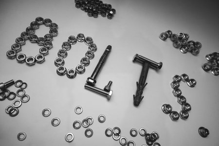 Creative composition of the word BOLTS made from hardware fasteners. Industrial background with scattered steel nuts, screws, and wall plugs on flat white surface.の写真素材