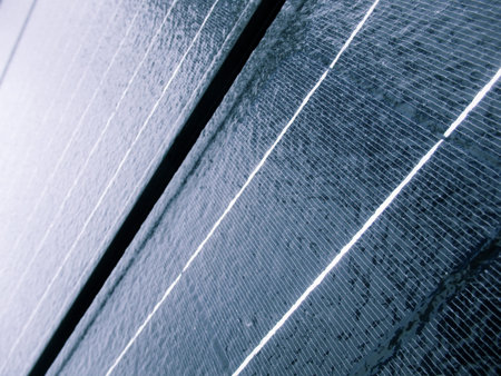 A close-up, angled view of a blue photovoltaic panel covered in frost and melting ice. Highlights...