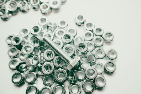 A single steel bolt placed on top of many stainless steel hexagonal nuts, providing a close-up view...