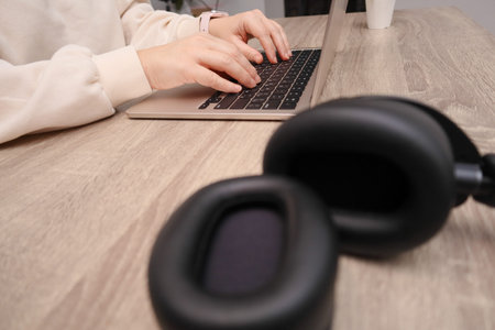 Close up of female hands working on a laptop in a bright room. Modern workspace with a wooden table,...