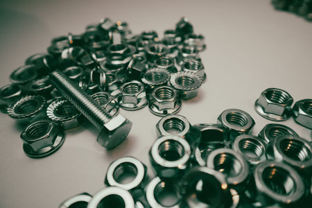 A single steel bolt placed on top of many stainless steel hexagonal nuts, providing a close-up view...