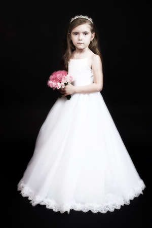 Cute girl with roses and in flower-girl dress  studio portrait on black background, old finishの写真素材