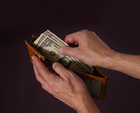 A man's hands hold open an old wallet with only three dollars left