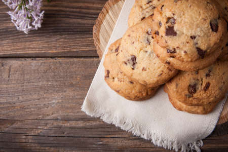 Stack of freshly baked chocolate chip cookies with glass of milk lying on linen napkin on rustic wooden tableの写真素材