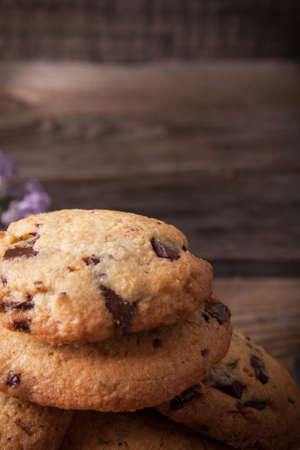 Stack of freshly baked chocolate chip cookies with glass of milk lying on linen napkin on rustic wooden tableの写真素材