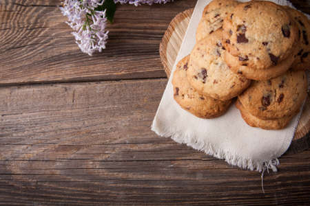 Stack of freshly baked chocolate chip cookies with glass of milk lying on linen napkin on rustic wooden tableの写真素材