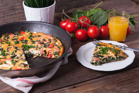 Pan of frittata with spinach, tomatoes and cheese on wooden table wiith orange juice. Portion on a plate.の写真素材