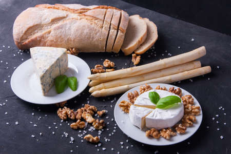 Blue cheese and camembert on plates with ciabatta, walnuts and asparagus, decorated with basilの写真素材