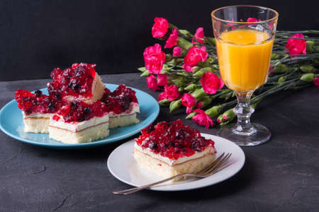 Piece of forest fruit cake with jelly and cream on a plate with orange juice. Stack of cake in the backgroundの写真素材