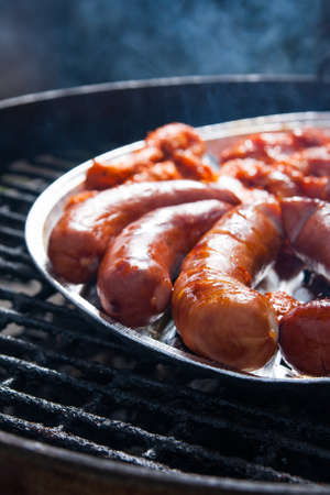 Tasty sausages and bacon on tray on grill outdoorの写真素材