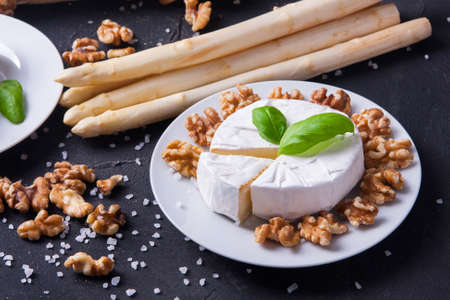 Blue cheese and camembert on plates with ciabatta, walnuts and asparagus, decorated with basilの写真素材