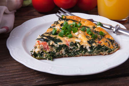 Plate of frittata with spinach, tomatoes and cheese on wooden table with orange juiceの写真素材