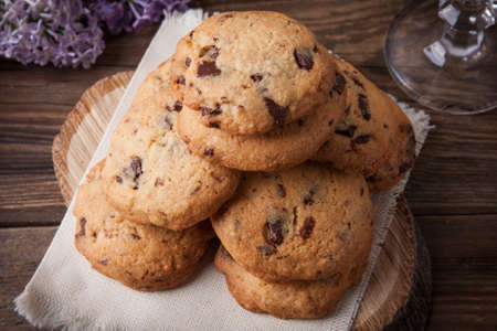 Stack of freshly baked chocolate chip cookies with glass of milk lying on linen napkin on rustic wooden tableの写真素材