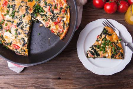 Pan of frittata with spinach, tomatoes and cheese on wooden table wiith orange juice. Portion on a plate.の写真素材