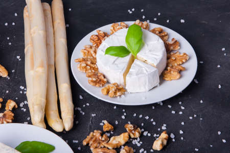 Blue cheese and camembert on plates with ciabatta, walnuts and asparagus, decorated with basilの写真素材
