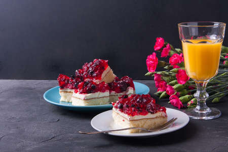 Piece of forest fruit cake with jelly and cream on a plate with orange juice. Stack of cake in the backgroundの写真素材