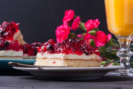 Piece of forest fruit cake with jelly and cream on a plate with orange juice. Stack of cake in the backgroundの写真素材