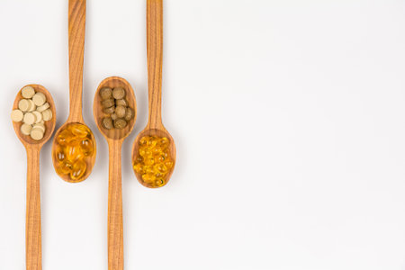 Dietary supplement capsules and herbal pills on wooden spoons, top view with copy spaceの写真素材
