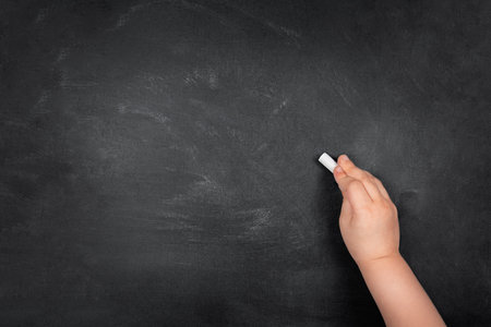 Child hand writing with chalk on empty school blackboard, copy spaceの写真素材