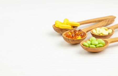 Vitamin pills and dietary supplements in wooden spoons on white wooden table, healthcare conceptの写真素材