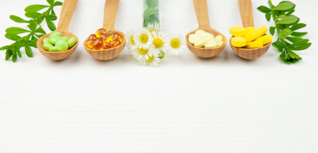 Wooden spoons with various vitamins, supplements and herbal capsules , green leaves and herbs in test tube on white tableの写真素材