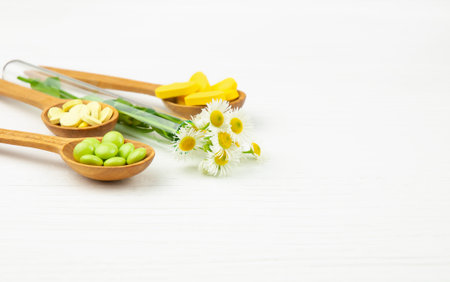 Various dietary supplements, vitamins and herbal pills on wooden spoons and chamomiles in test tube on white wooden background. alternative medicine conceptの写真素材