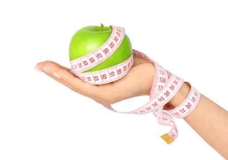 Female hand holding green apple wrapped with measuring tape isolated on white background. weight loss and dieting conceptの写真素材