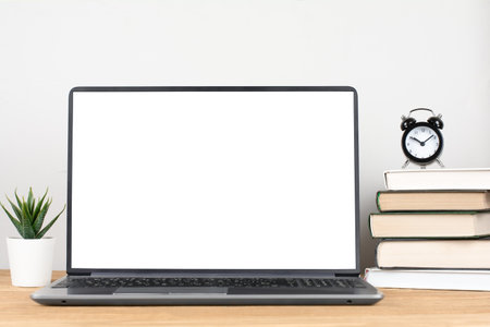 Laptop with blank screen on wooden table with stack of books, alarm clock and green plantの写真素材