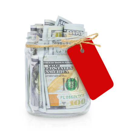 Glass jar with dollars and blank red paper tag isolated on white backgroundの写真素材