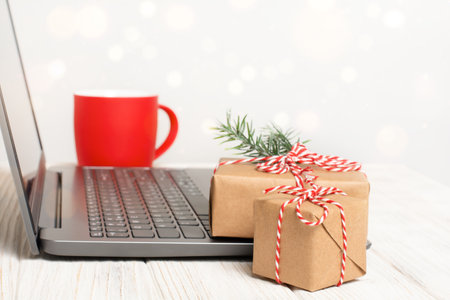 Christmas gift boxes and cup near the laptop on white table. Working place with defocused lights and copy space. Online shopping or greeting conceptの写真素材