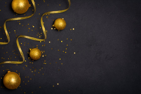 Golden Christmas ornament, ribbons and glittering star confetti on black background. Top view with copy spaceの写真素材