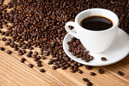Scattered coffee beans and cup with coffee on wooden backgroundの写真素材