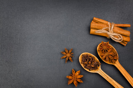 Cinnamon sticks, star anise and cloves in wooden spoons on black background. Top view with copy space, flat layの写真素材