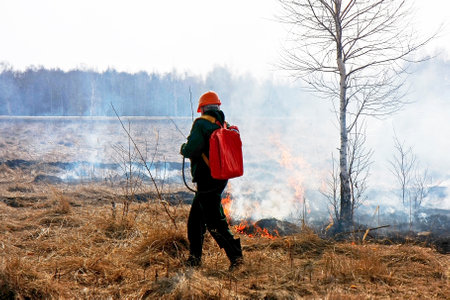 A firefighter in a field extinguishes a fire with water.の写真素材