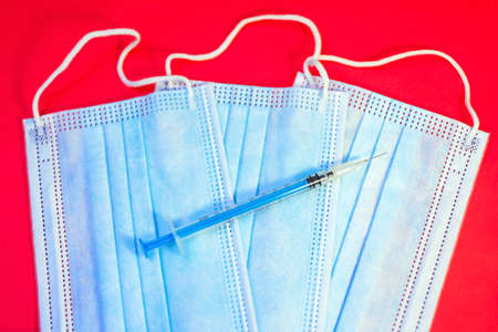 A blue mask with a white background and a syringe for injection for healthcare workers and people at risk. Treatment by vaccination against SARS-CoV-2. copyspace.の写真素材