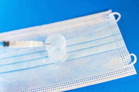 A blue mask with a blue background and a syringe for injection for healthcare workers and people at risk. Treatment by vaccination against SARS-CoV-2. copyspace.の写真素材