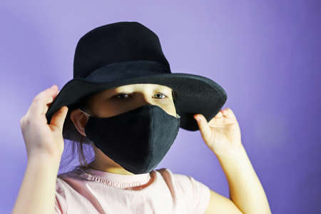 Girl in a black hat and black mask on a purple background